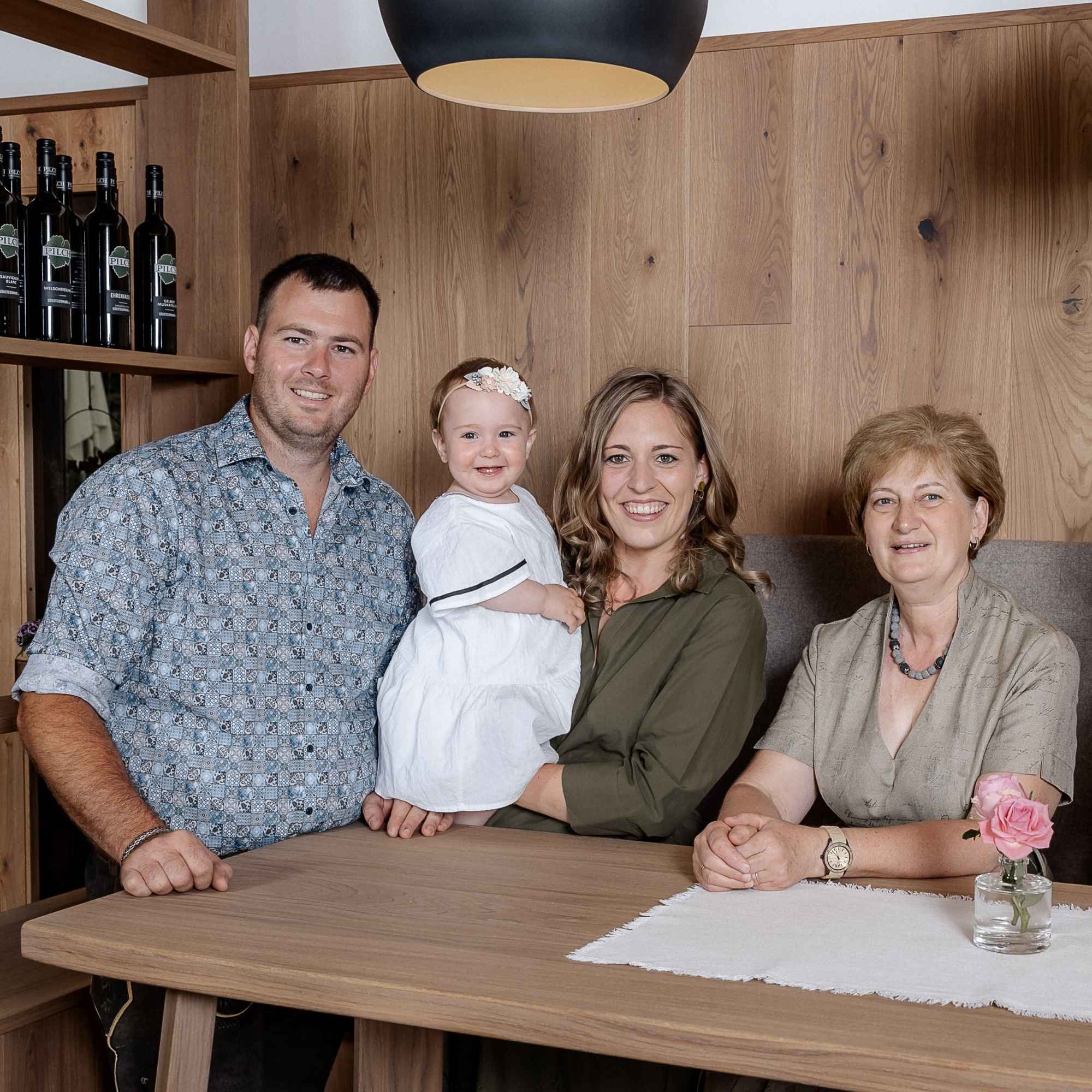 Drei Generationen der Winzerfamilie Pilch im Weingut Pilch in der Südsteiermark. Gemeinsames Familienporträt im Verkostungsraum mit Weinflaschen aus eigener Produktion und gemütlicher Holzatmosphäre.